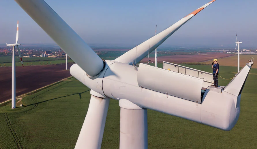 Ingenieur steht mit PSA auf Windkraftanlage und schaut durch die aufgeklappt Gondel auf das Getriebe