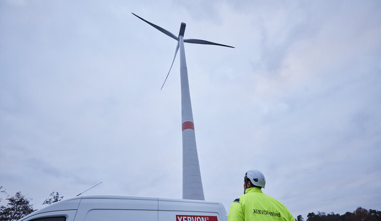 Equipmentfahrzeu und Mitarbeiter vor Windkraftanlage