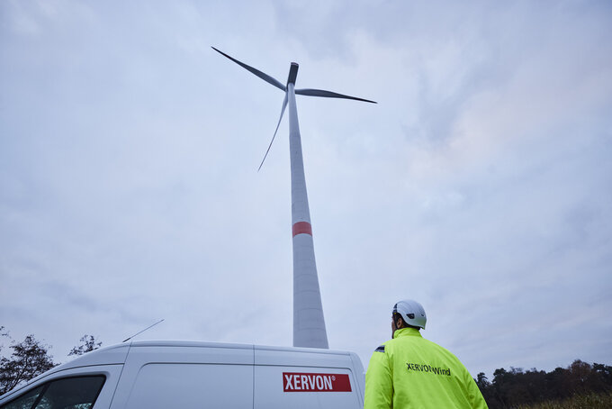 Equipmentfahrzeu und Mitarbeiter vor Windkraftanlage